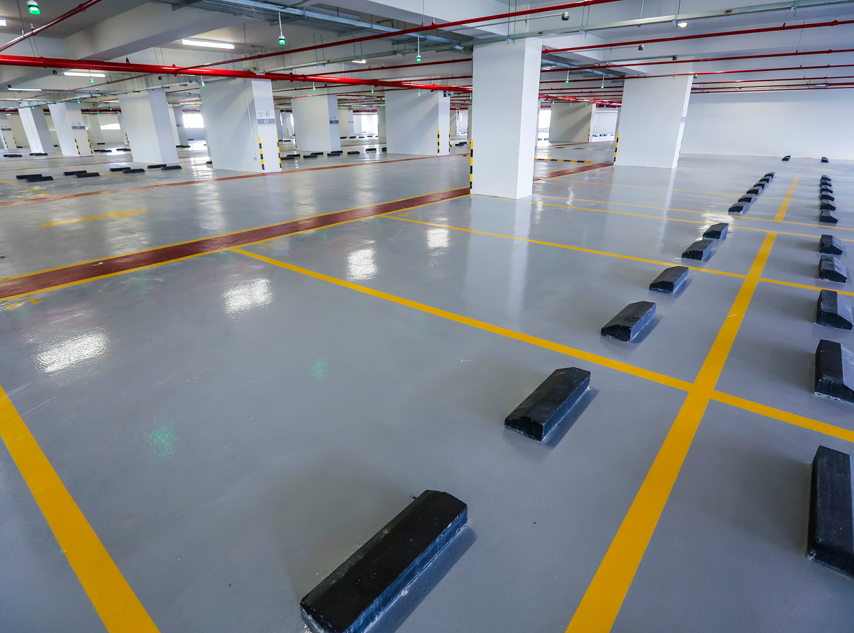 Large warehouse with a lot of black and yellow lines on the floor, black objects, pillars, lights, and pipes