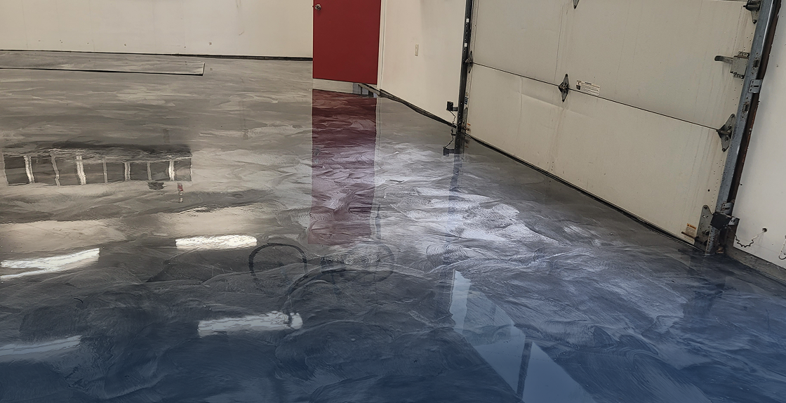 Garage floor with a red door and a white wall, and the floor is covered in a blue epoxy coating