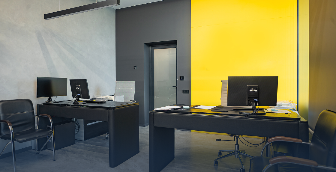 Modern office with two desks and chairs in front of a yellow wall