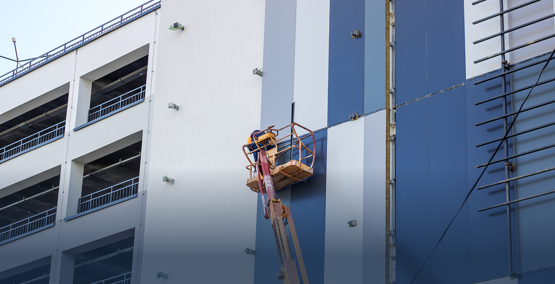 Man in a cherry picker working on the side of a building, with a crane in the foreground