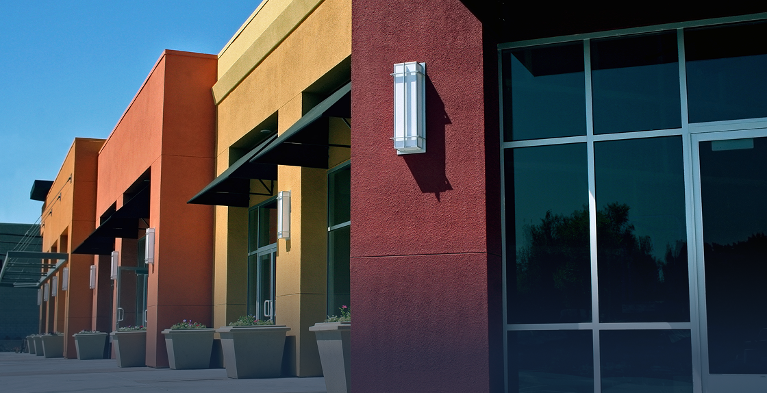 Row of colorful buildings with glass windows and doors, potted plants, and a clear blue sky in the background