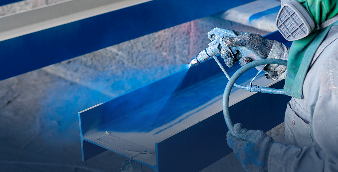 Man wearing a mask and gloves, holding a spray gun and spraying a blue paint onto a metal object