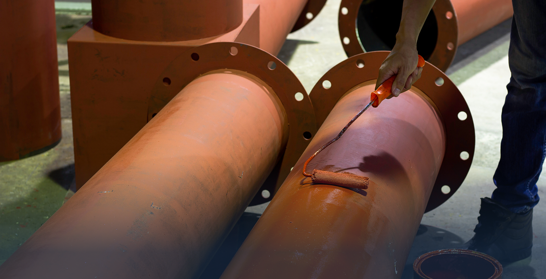 Man standing next to a large brown pipe, holding a tool in his hand