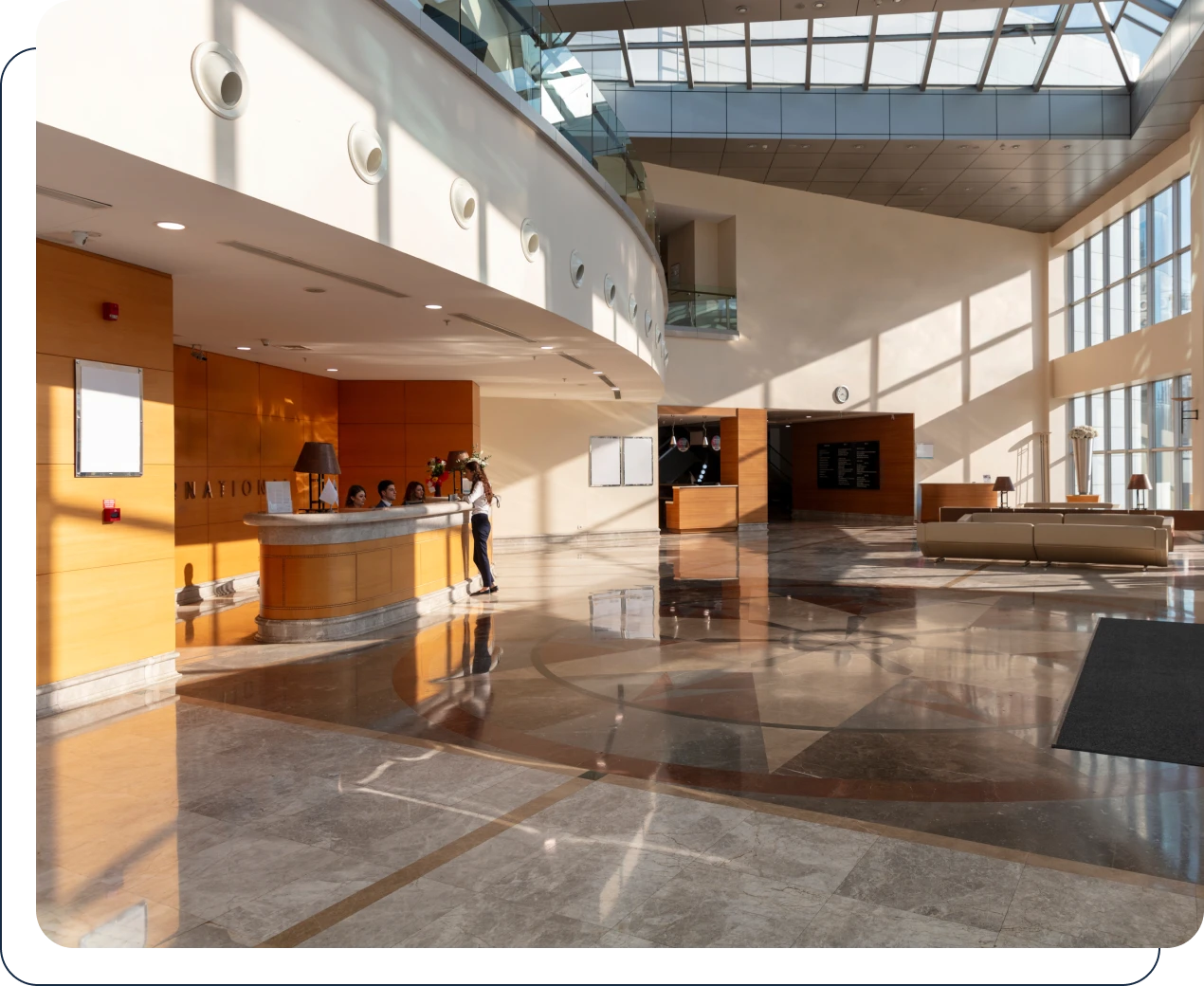 Lobby of a building with a large glass roof, a group of people standing on the floor