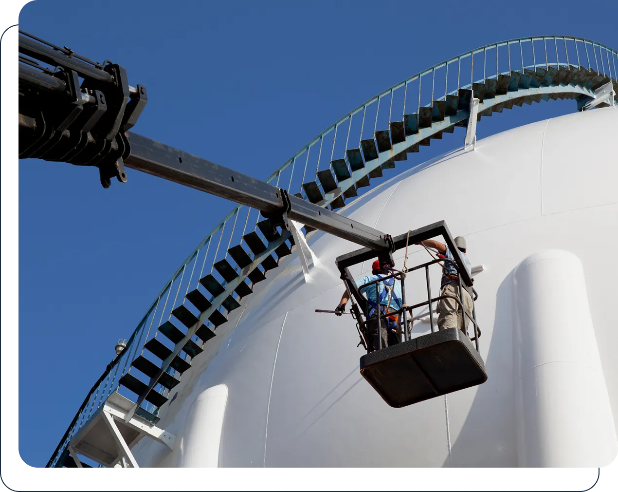 Workers power washing large white industrial tank